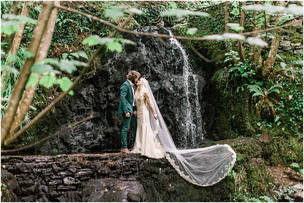 wedding couple with long veil standing in front of waterfall