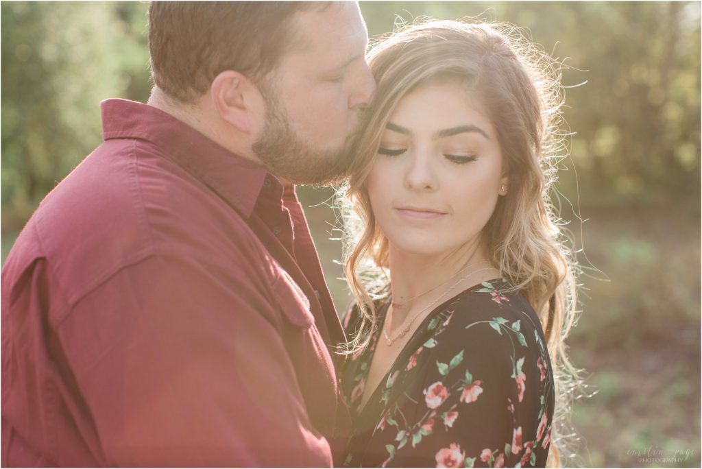 man kissing woman on temple in field engagement session