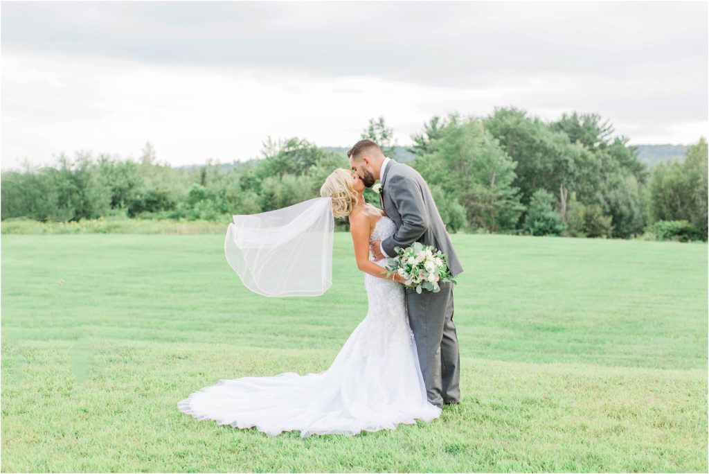 bride and groom kissing in field flying veil