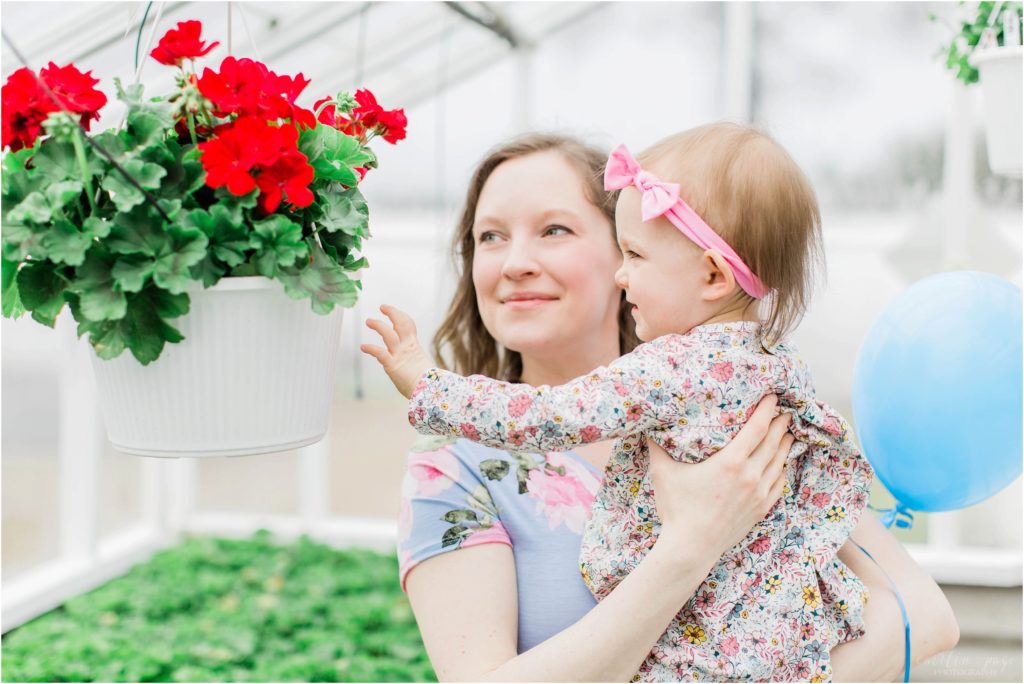 mom holding little girl looking at red flowers