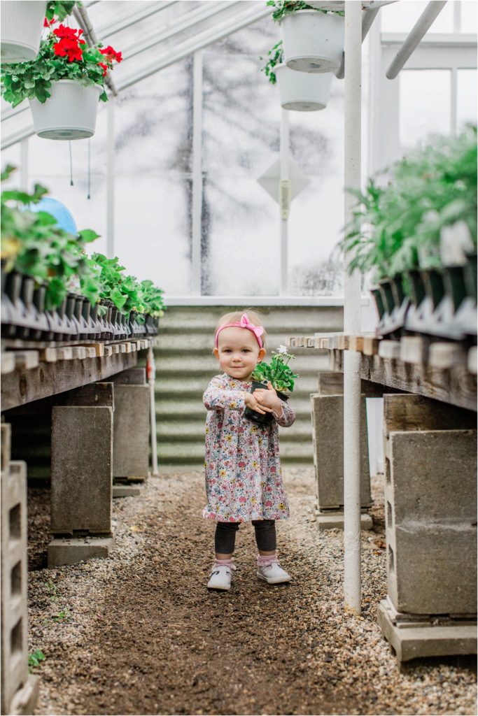 toddler girl standing in plant nursery aisle