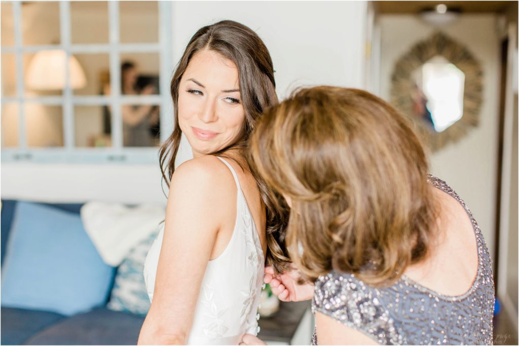 bride looking at mom while zipping her dress