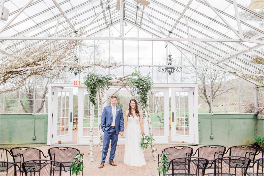 bride and groom standing under arbor in greenhouse