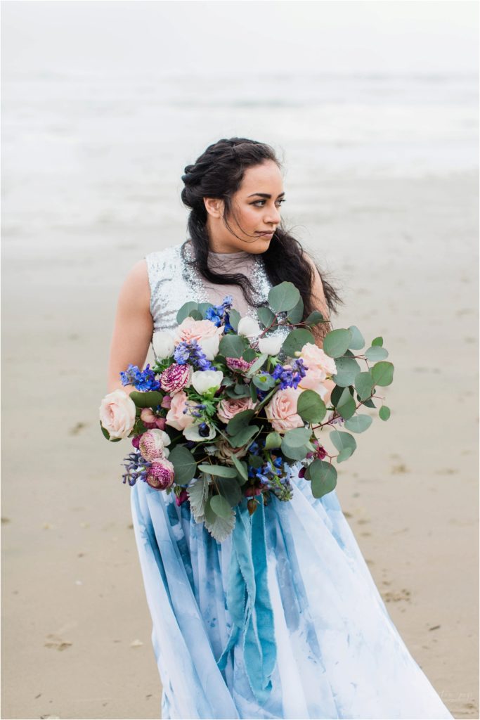 Bride holding textured bouquet with pink roses and anemones on Cannon Beach in Oregon