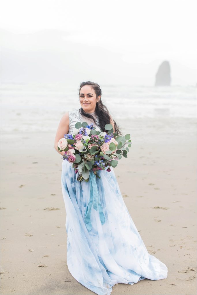 Bride holding textured bouquet with pink roses and anemones on Cannon Beach in Oregon
