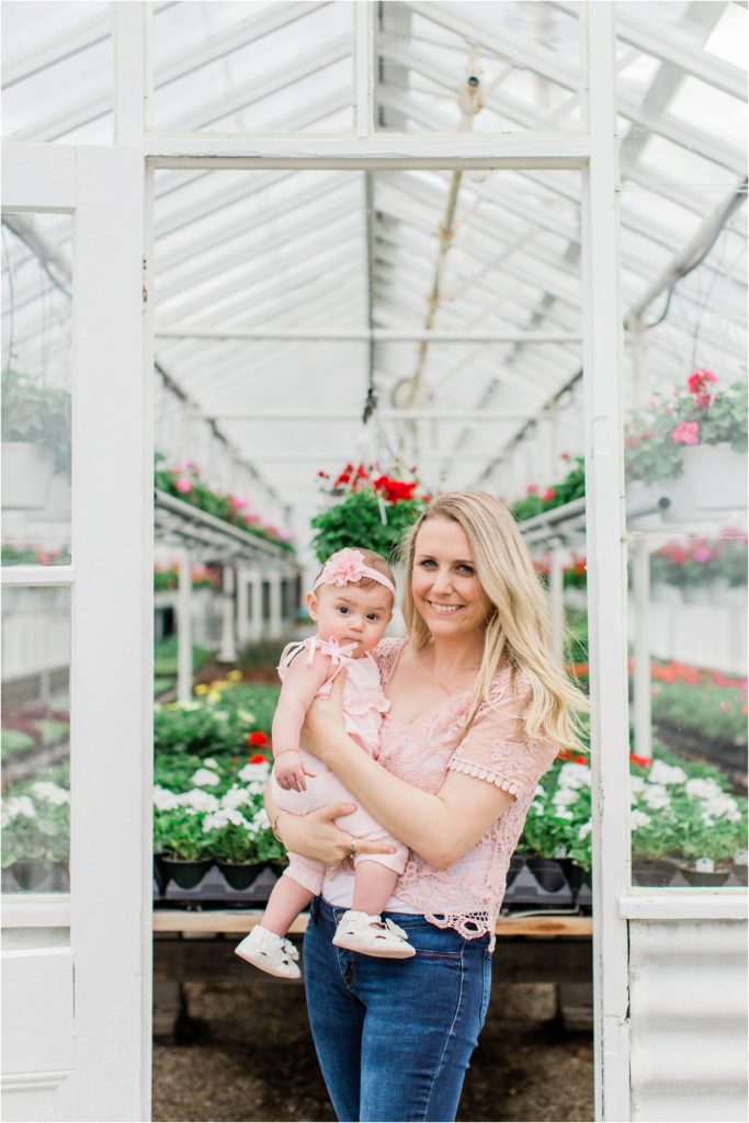 mom and baby girl in pink smiling outside of greenhouse