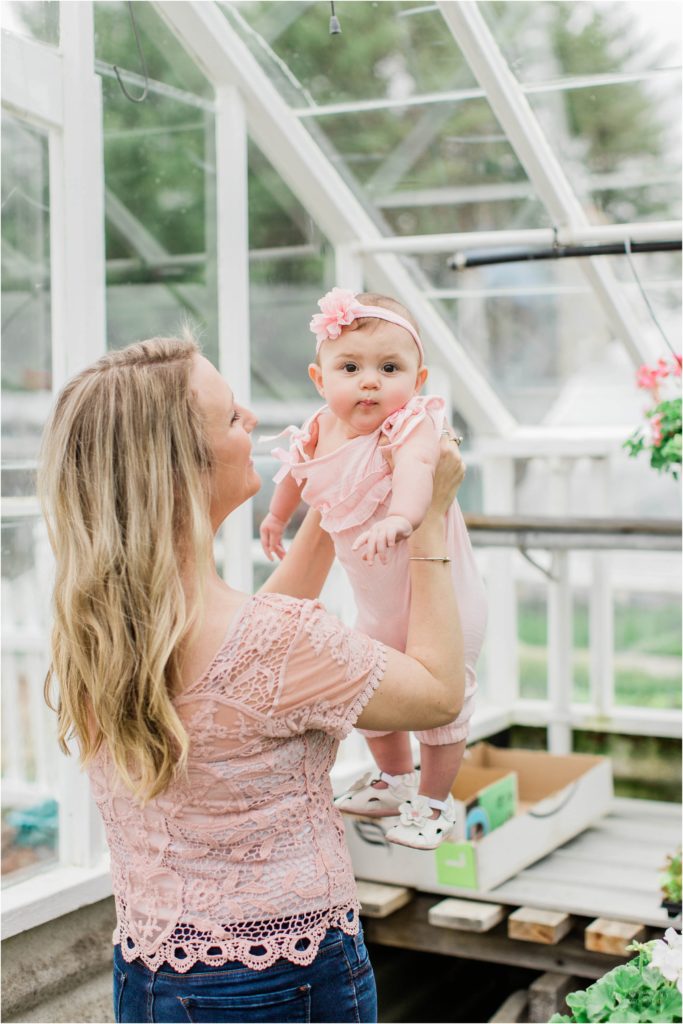 mom holding baby girl in the air in greenhouse