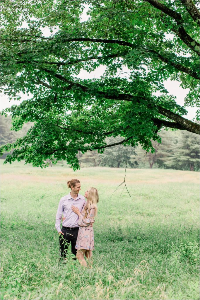 Man and woman standing in field under large maple tree