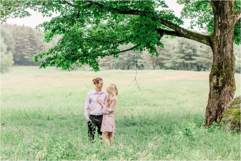 Man and woman standing in field under large maple tree