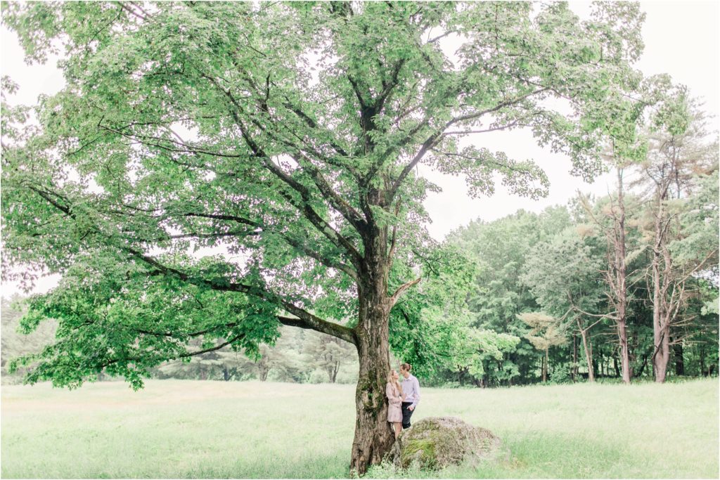 Man and woman standing on large rock under old maple tree