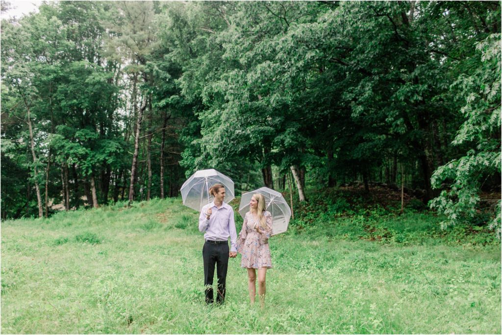 Man and woman standing together in field with clear umbrellas