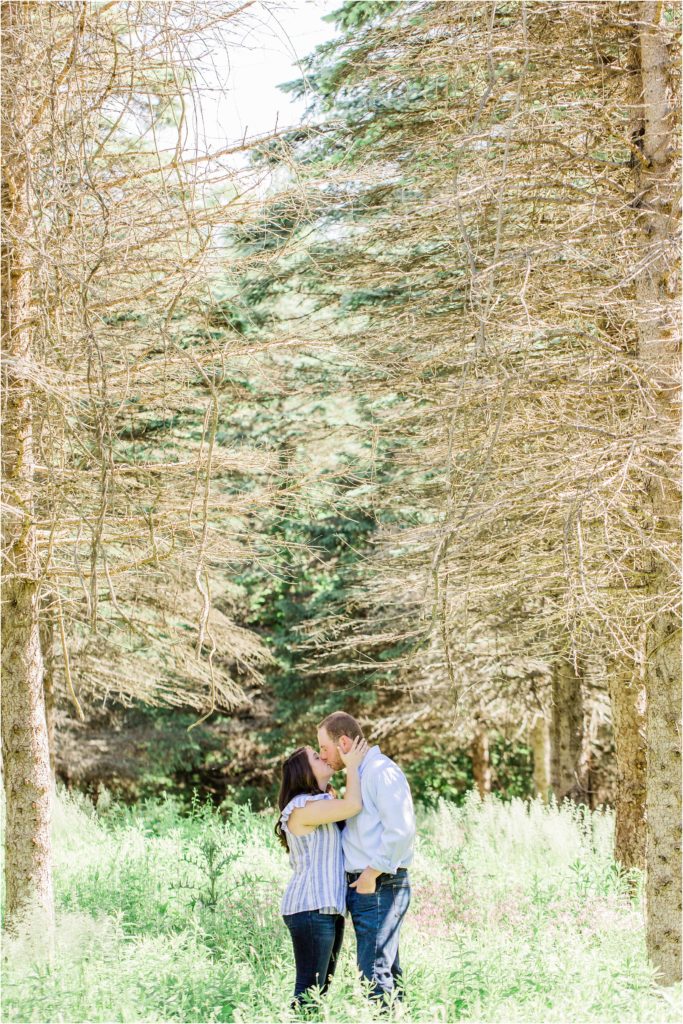 man and woman kissing between pine trees