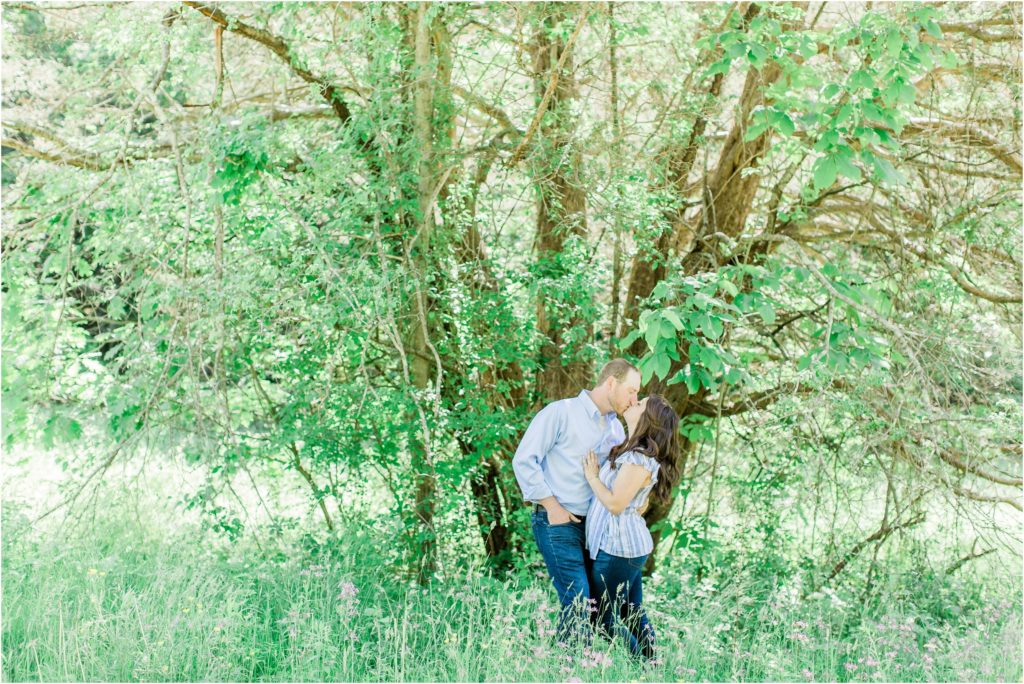man and woman kissing in front of large tree
