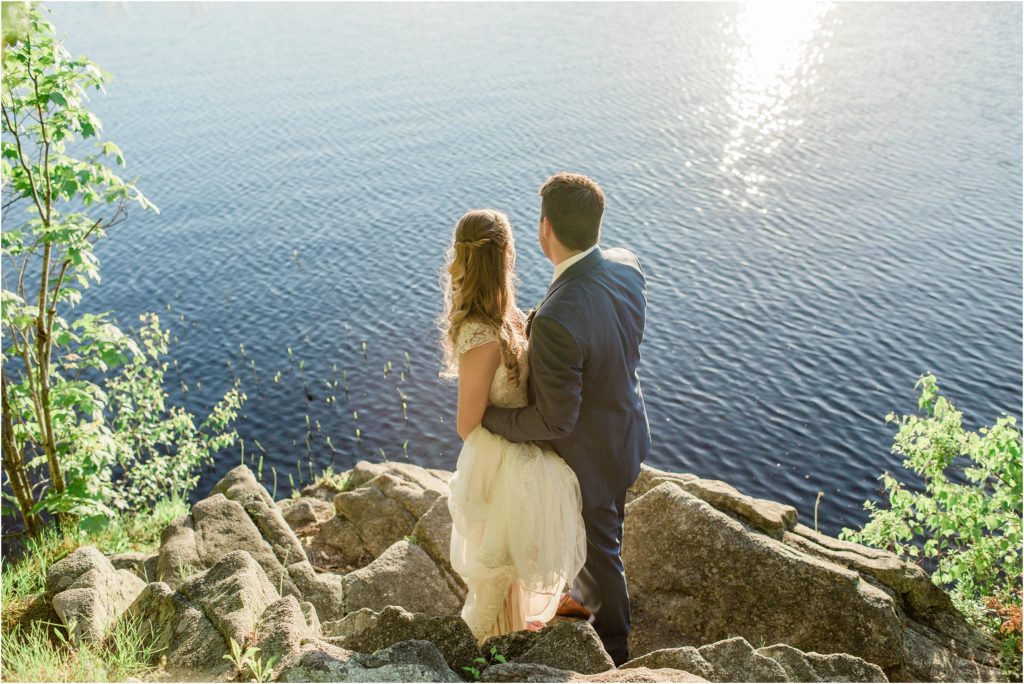 bride and groom standing on rocks looking at sunset