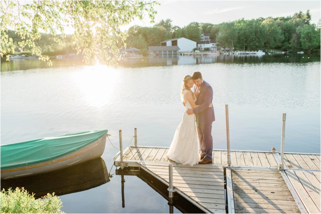 bride and groom standing on dock at sunset with boat
