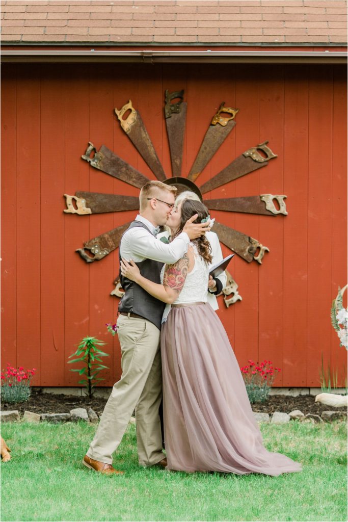 bride and groom first kiss in front of red barn
