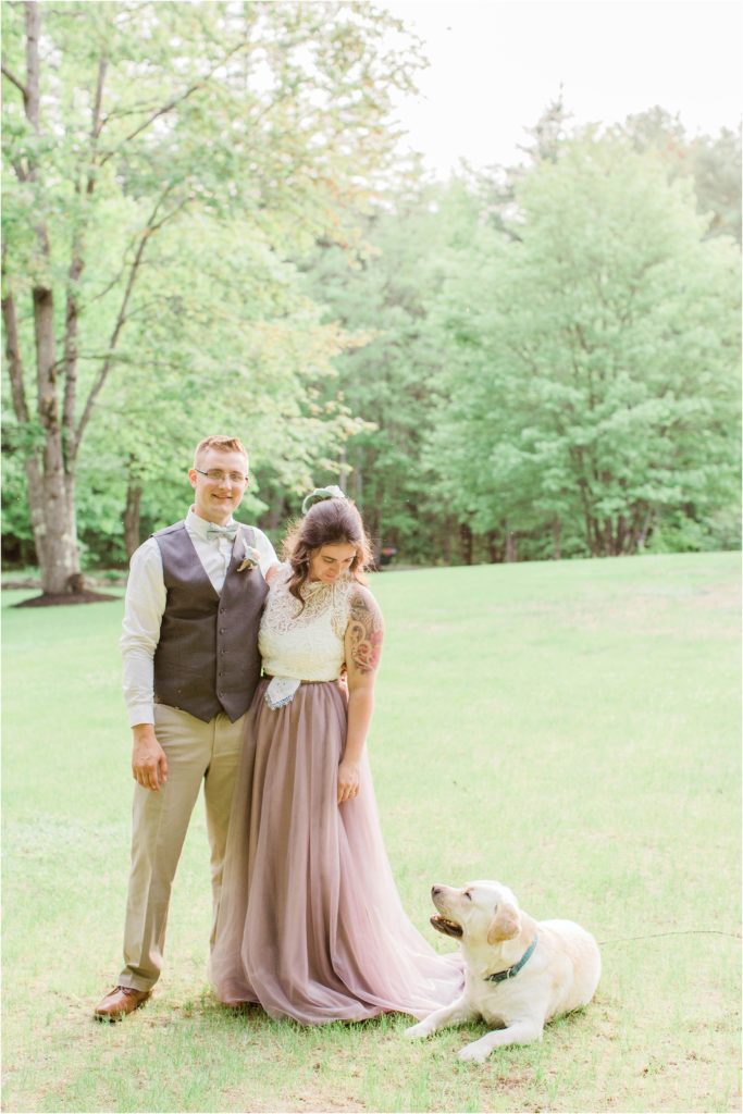 bride and groom standing at sunset with dog laying on skirt