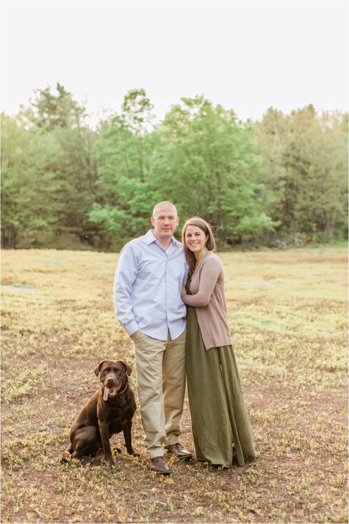 couple standing in field with chocolate lab
