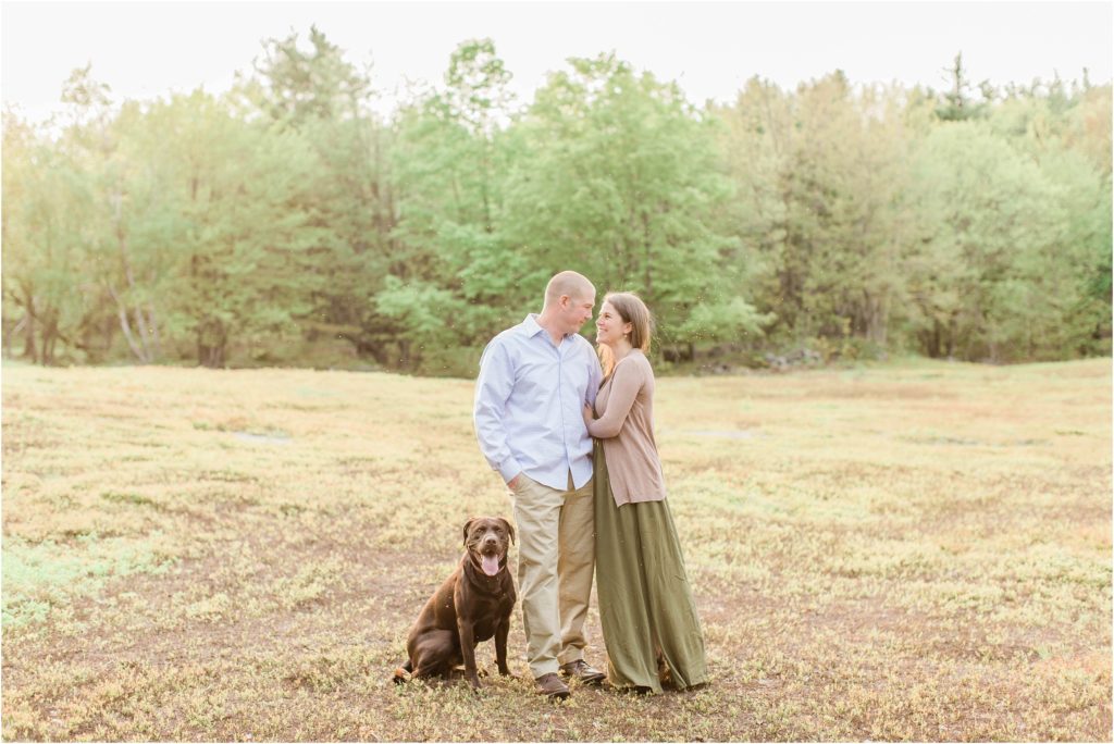 couple kissing in field with chocolate lab