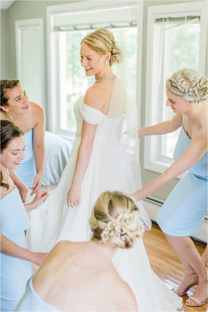 Bridesmaids gathered around bride holding her dress