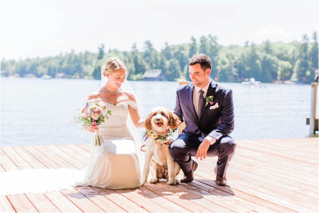 Bride and groom squatting on dock with dog ring bearer