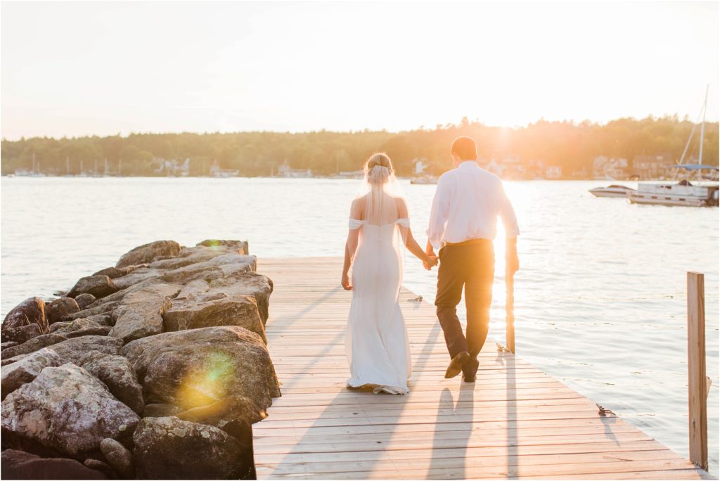 Sunset portraits of bride and groom walking down dock at Brewster Boathouse Wolfeboro New Hampshire