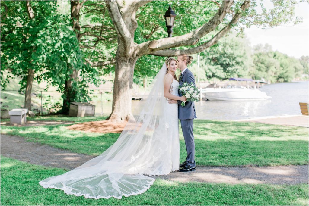 bride and groom standing under a tree with long veil