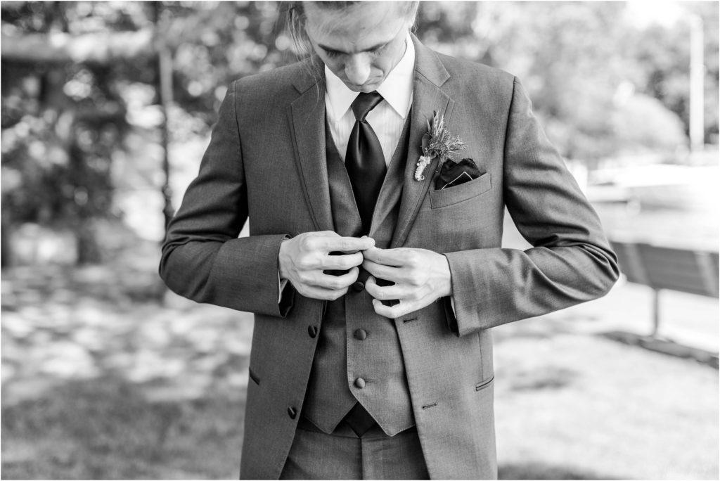 black and white portrait of groom buttoning jacket
