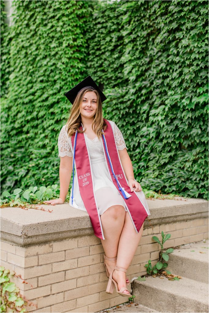 Senior girl sitting in front of ivy with cap and sash
