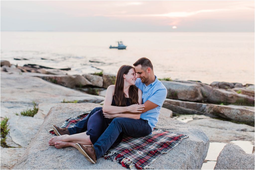 Couple sitting together on rocks at sunset with lobster boat in background