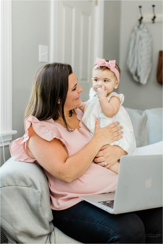 Mom holding baby girl and working on laptop