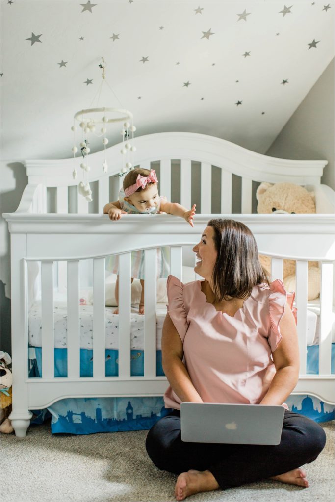 Woman working on laptop and sitting in front of baby's crib