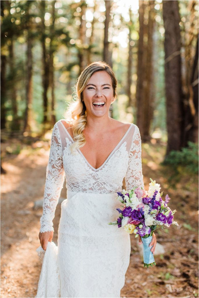 Bride holding onto her bouquet and standing in trees laughing