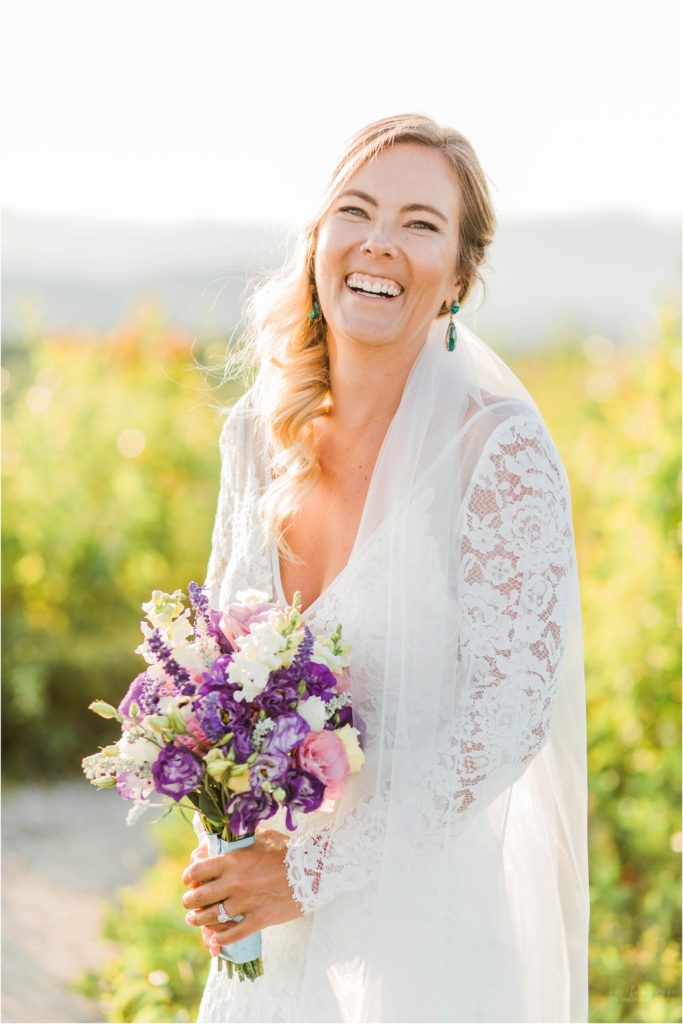 Bride in wedding dress and veil holding her pink and purple bouquet on top of Foss Mountain