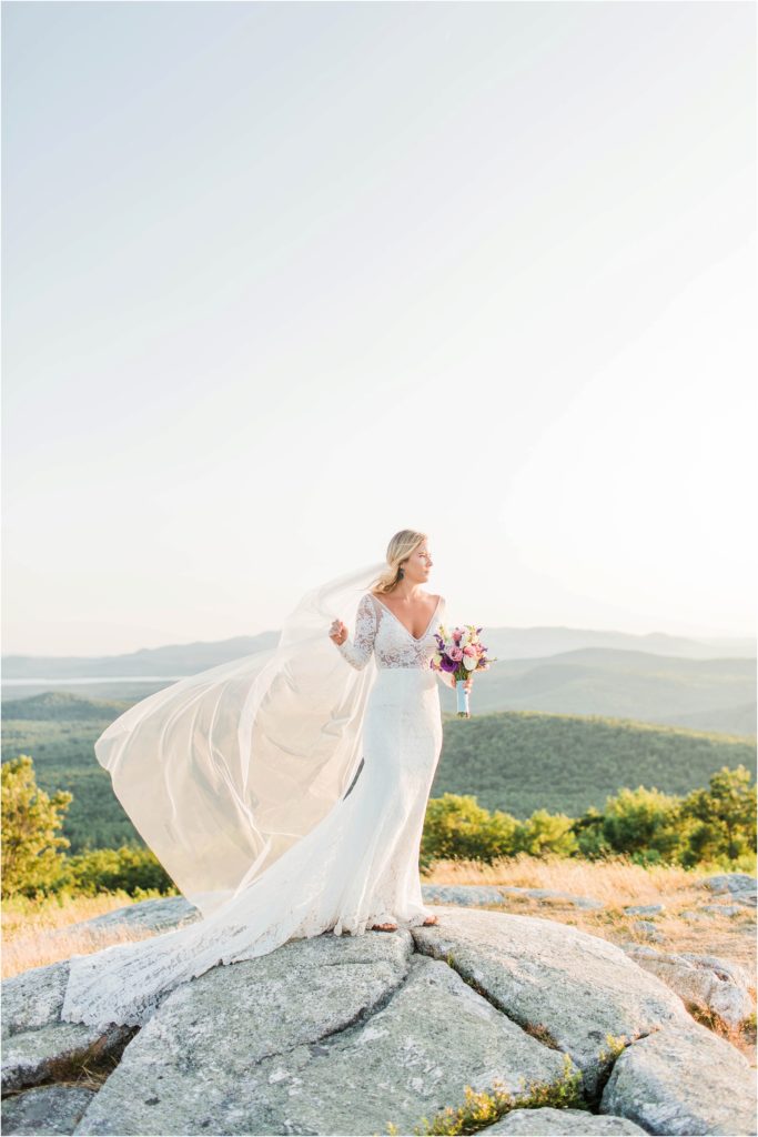 Bride standing on top of Foss Mountain at sunset with long veil and bouquet