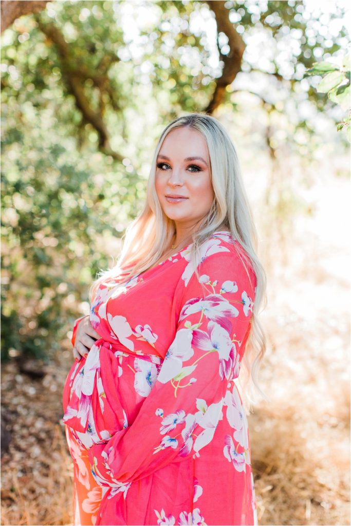 Pregnant woman in pink flowered dress standing under tree at sunset Coto de Caza California