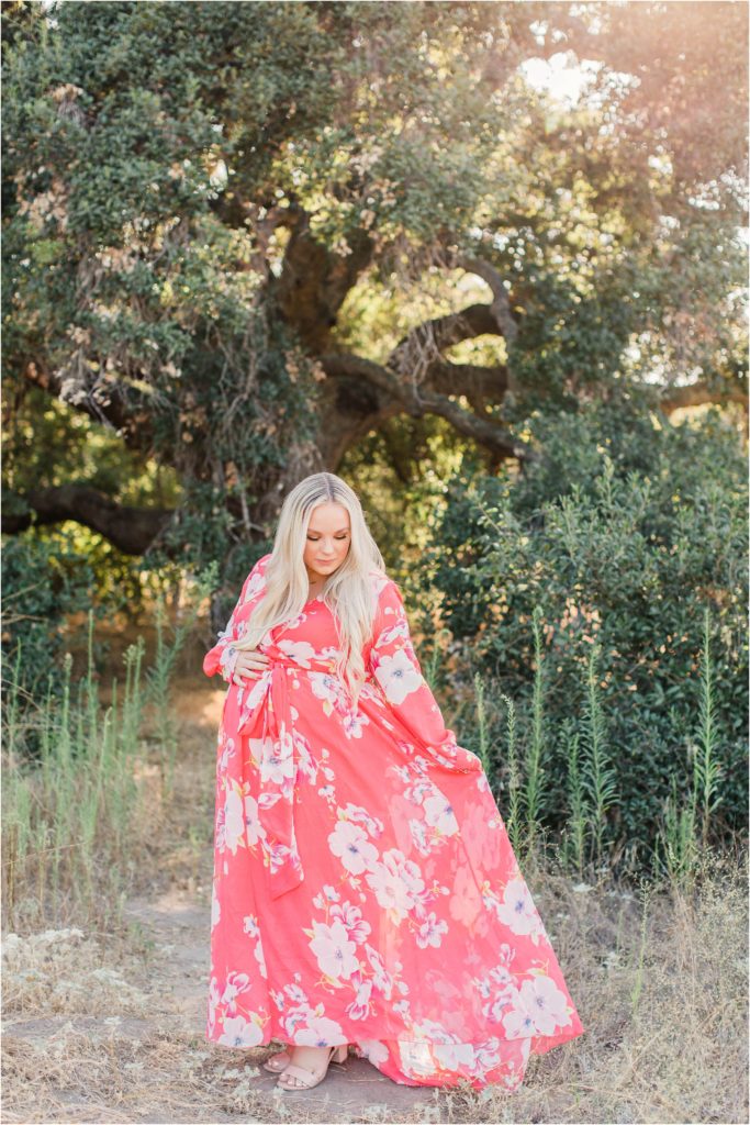 Pregnant woman in pink flowered dress standing under tree at sunset Coto de Caza California