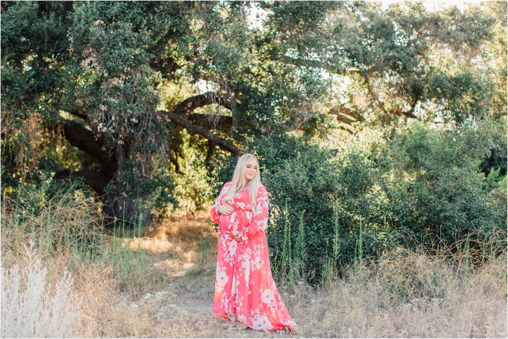 Pregnant woman in pink flowered dress standing under tree at sunset Coto de Caza California