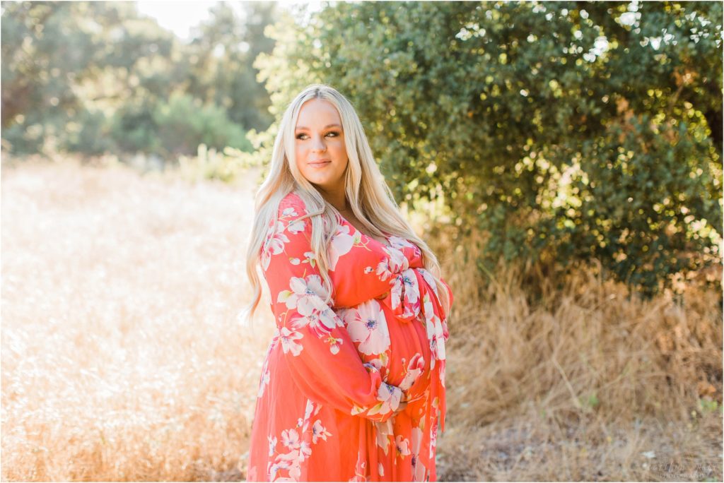 Pregnant woman standing next to tree in pink dress at sunset