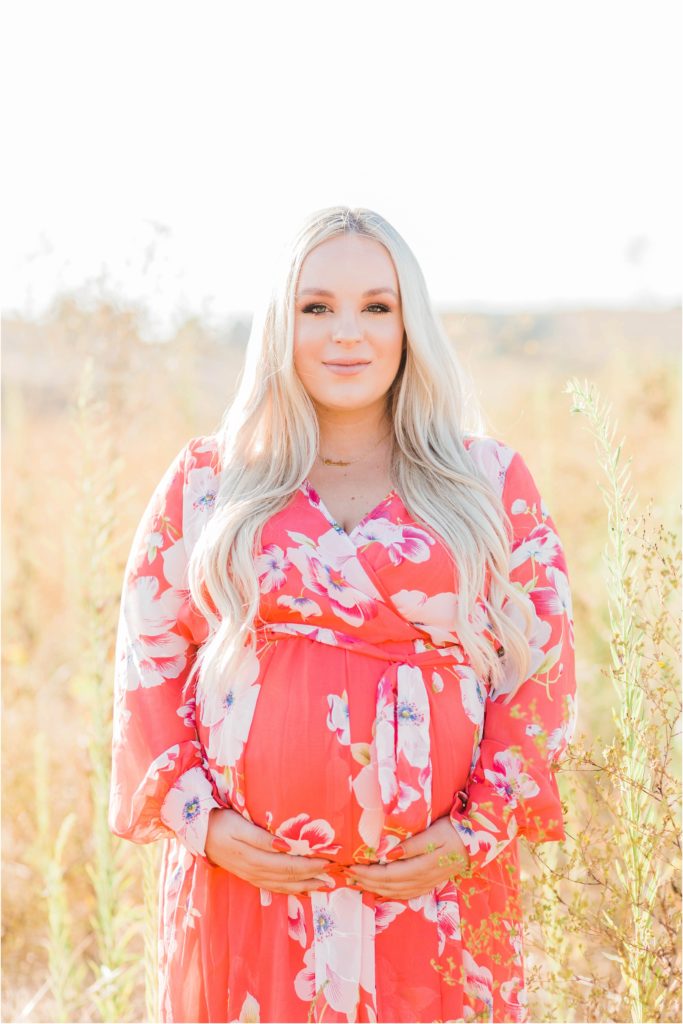 Pregnant woman in pink dress at sunset in field