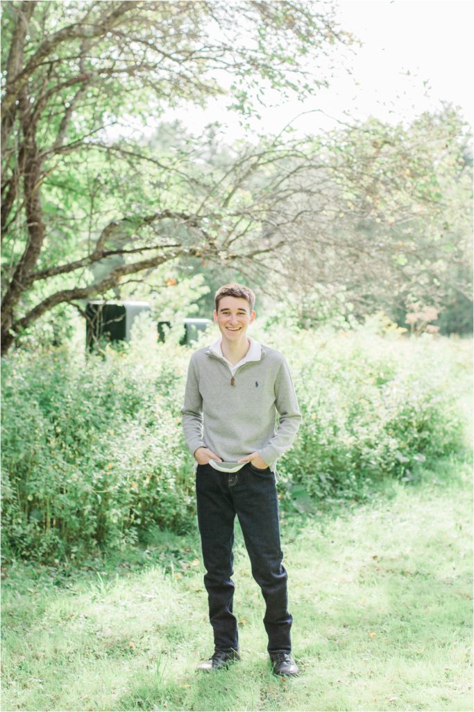 senior boy standing in field in front of tree
