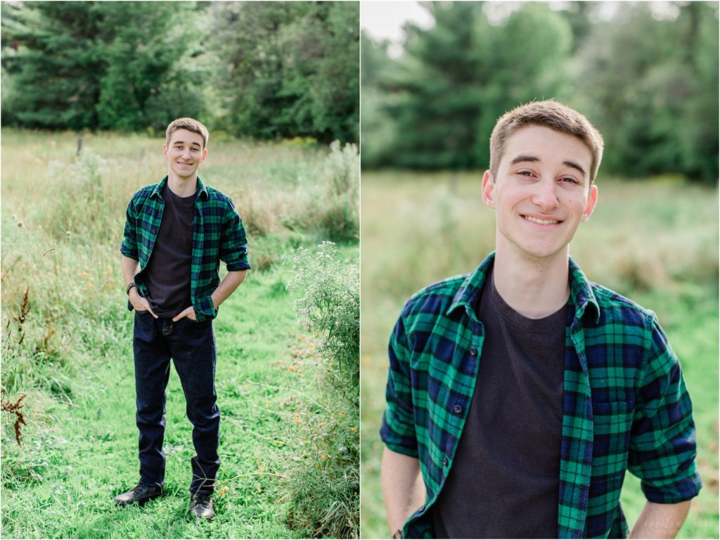 senior boy standing in field in green and black flannel