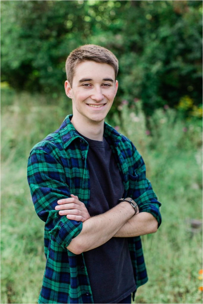 senior boy standing in field in checkered flannel shirt