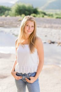 senior girl standing on riverbank at sunset