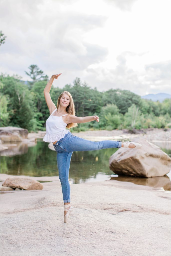 senior girl doing arabesque on rocks at riverside