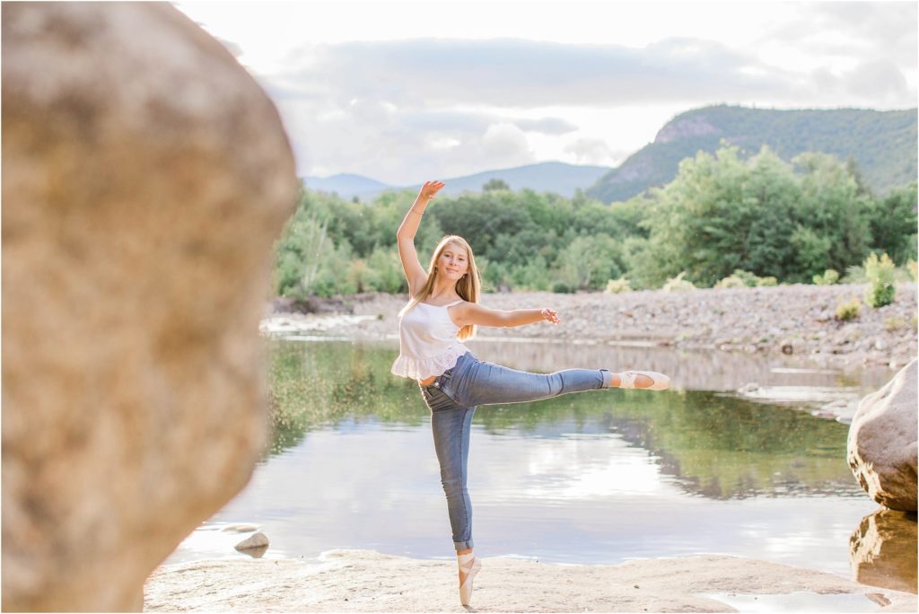 senior girl doing arabesque on rocks at riverside