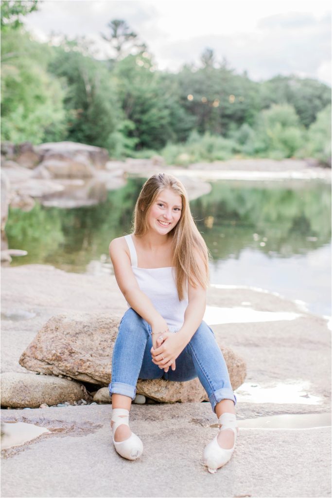 senior girl sitting on rock with pointe shoes on