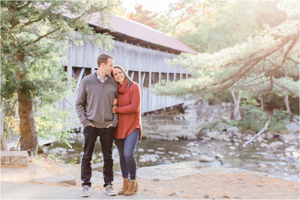 couple standing in front of covered bridge at sunset