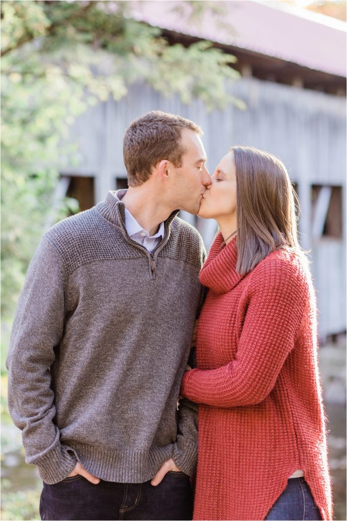 couple kissing in front of covered bridge at sunset