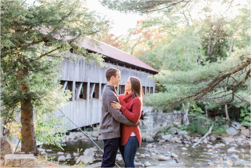 couple standing in front of covered bridge at sunset